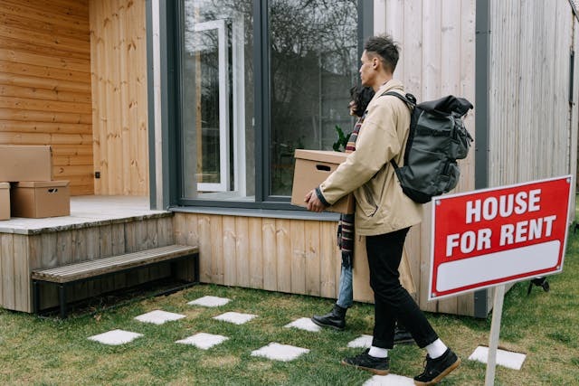 people moving boxes into a house with a for rent sign